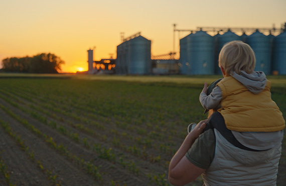Child sitting on fathers shoulder walking through a field admiring sunset